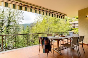A balcony with a table set for two, overlooking a forested hillside.