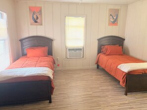 Een kamer met twee bedden, een raam met zonwering en een luchtkoeler aan de muur.