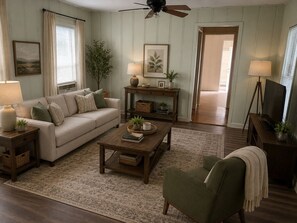 A living room with a sofa, coffee table, armchair, and a television on a stand.