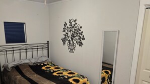 A bedroom with a bed, a bedside table, a wall-mounted mirror, and a ceiling light fixture.