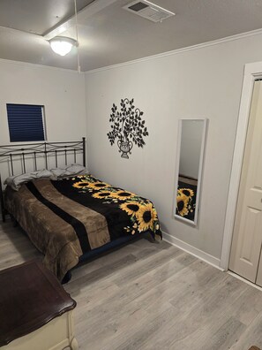 A bedroom with a bed, a bedside table, a wall-mounted mirror, and a ceiling light fixture.