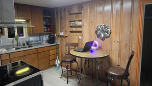 A kitchen with wooden cabinets, a stove, a sink, a coffee maker, and a laptop on a table with bar stools.