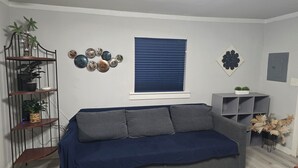 A living room with a grey sofa, a blue window, wall decor, and a plant shelf.