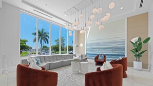 A modern living room with a large window, a sofa, two armchairs, a coffee table, and pendant lighting. - 🌴 Olde Naples Luxury at The Mark | Walk to Beach + 5th Ave | Weekly Stays | Resort Pool & Spa (Naples)