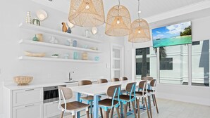 A modern kitchen with white cabinets, a dining area with blue chairs, and a large window with a view of the ocean. - 🌴 Olde Naples Luxury at The Mark | Walk to Beach + 5th Ave | Weekly Stays | Resort Pool & Spa (Naples)