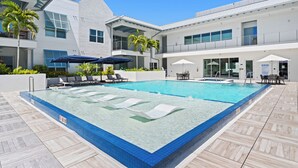 A swimming pool with lounge chairs, umbrellas, and a modern building with balconies. - 🌴 Olde Naples Luxury at The Mark | Walk to Beach + 5th Ave | Weekly Stays | Resort Pool & Spa (Naples)