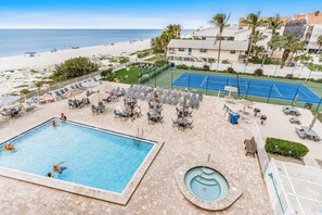 A pool area with a hot tub, lounge chairs, and a tennis court. - Reef Club 302 Gulf View Condo w/ Pool, Beach Access, Tennis & Sunsets (Indian Rocks Beach)