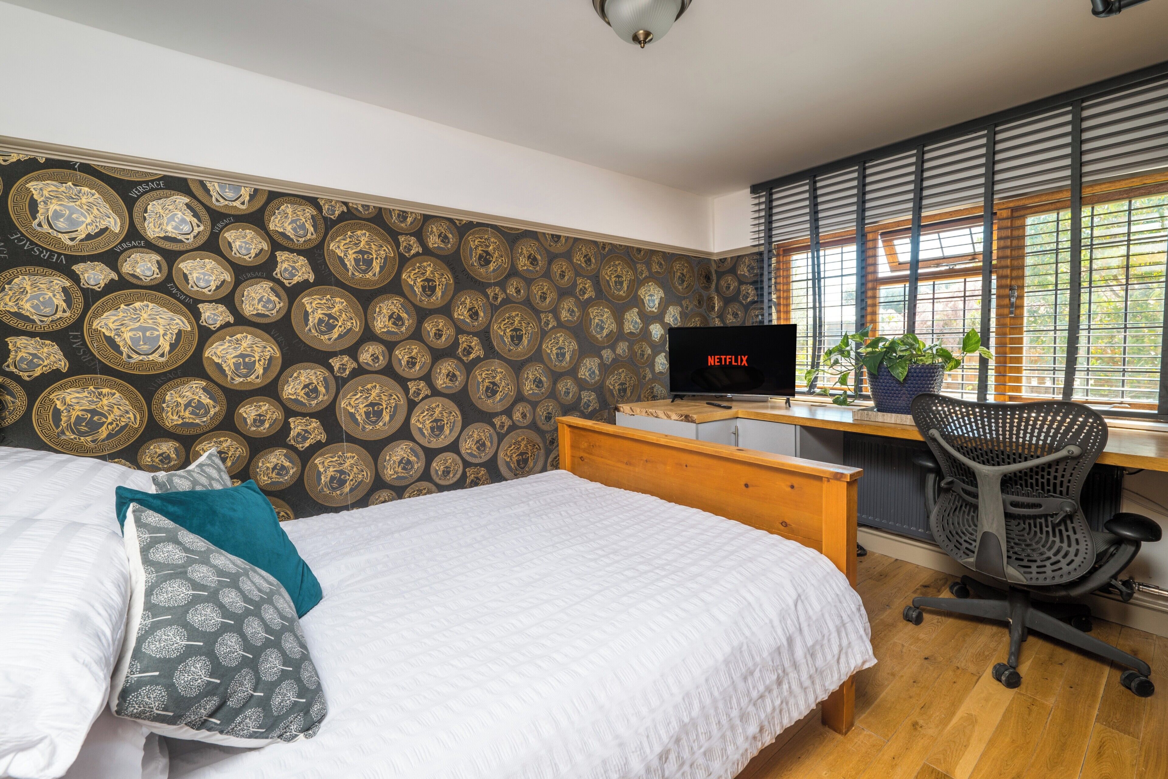 A bedroom with a bed, a desk with a computer, a chair, and a window with blinds.