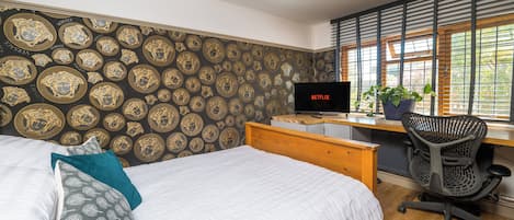 A bedroom with a bed, a desk with a computer, a chair, and a window with blinds.