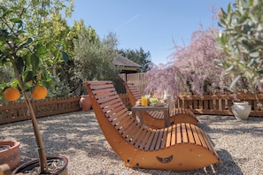 Un fauteuil de jardin en bois, accompagné d’une table, entouré de plantes en pot et d’une clôture en bois.