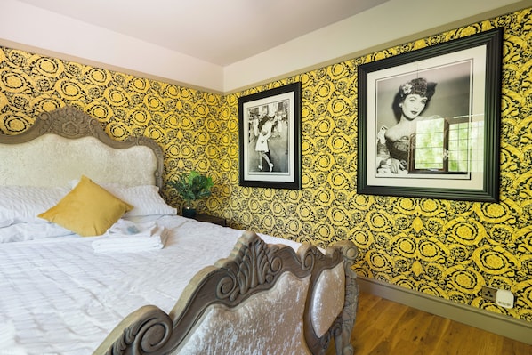 Une chambre à coucher avec un lit, une tête de lit, un papier peint jaune à motifs et deux tableaux encadrés accrochés au mur.
