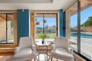A modern room with large windows, a pool view, and a table with chairs. - Desert Valley Retreat 3BD - Pool + Putting Green (Phoenix)