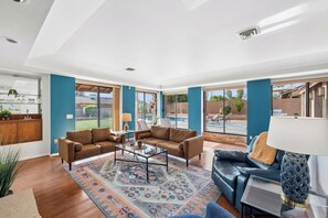 A spacious living room with a large window, a blue sofa, a brown sofa, a coffee table, and a patterned rug. - Desert Valley Retreat 3BD - Pool + Putting Green (Phoenix)
