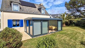 Une maison moderne dotée d’une véranda en verre, d’un toit en pente et d’une pelouse bien entretenue.