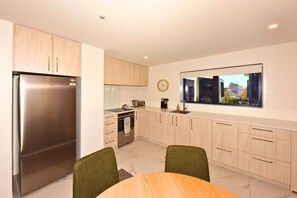 Eine moderne Küche mit einem Edelstahlkühlschrank, Holzschränken, einem eingebauten Backofen und einem Fenster mit Blick auf die Stadt.