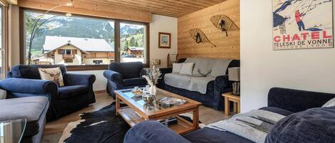 A cozy living room with a wooden ceiling, large windows, and a mountain view.