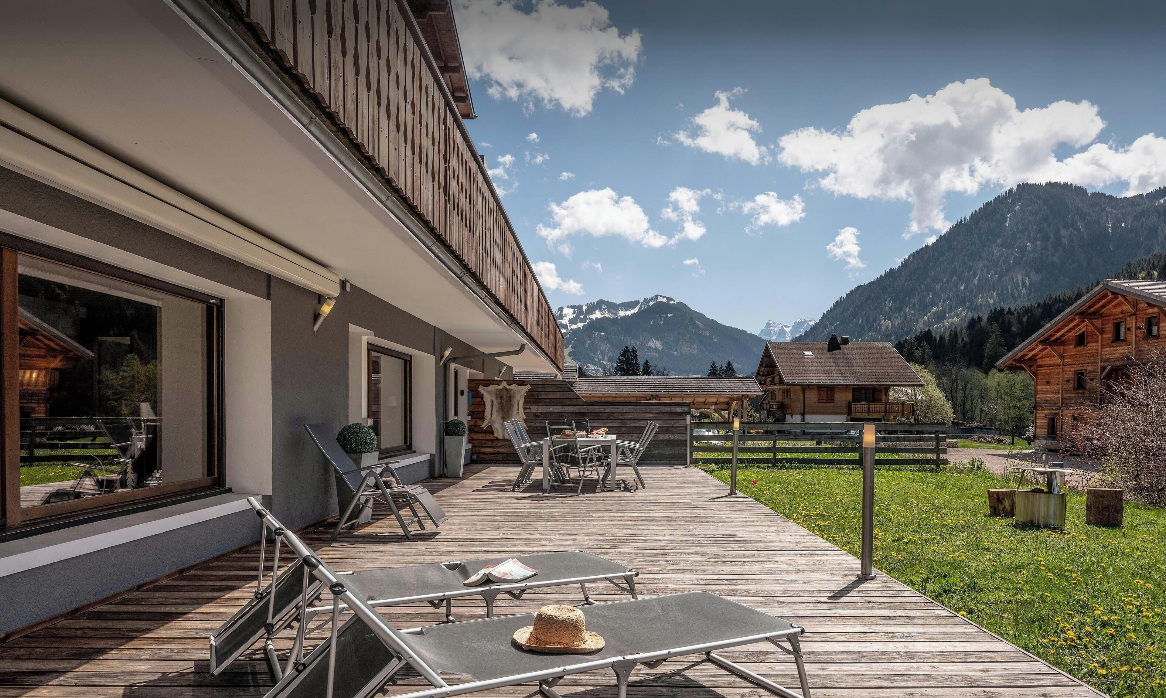 Una terraza de madera con sillones de descanso, zona de comedor y vistas a montañas.