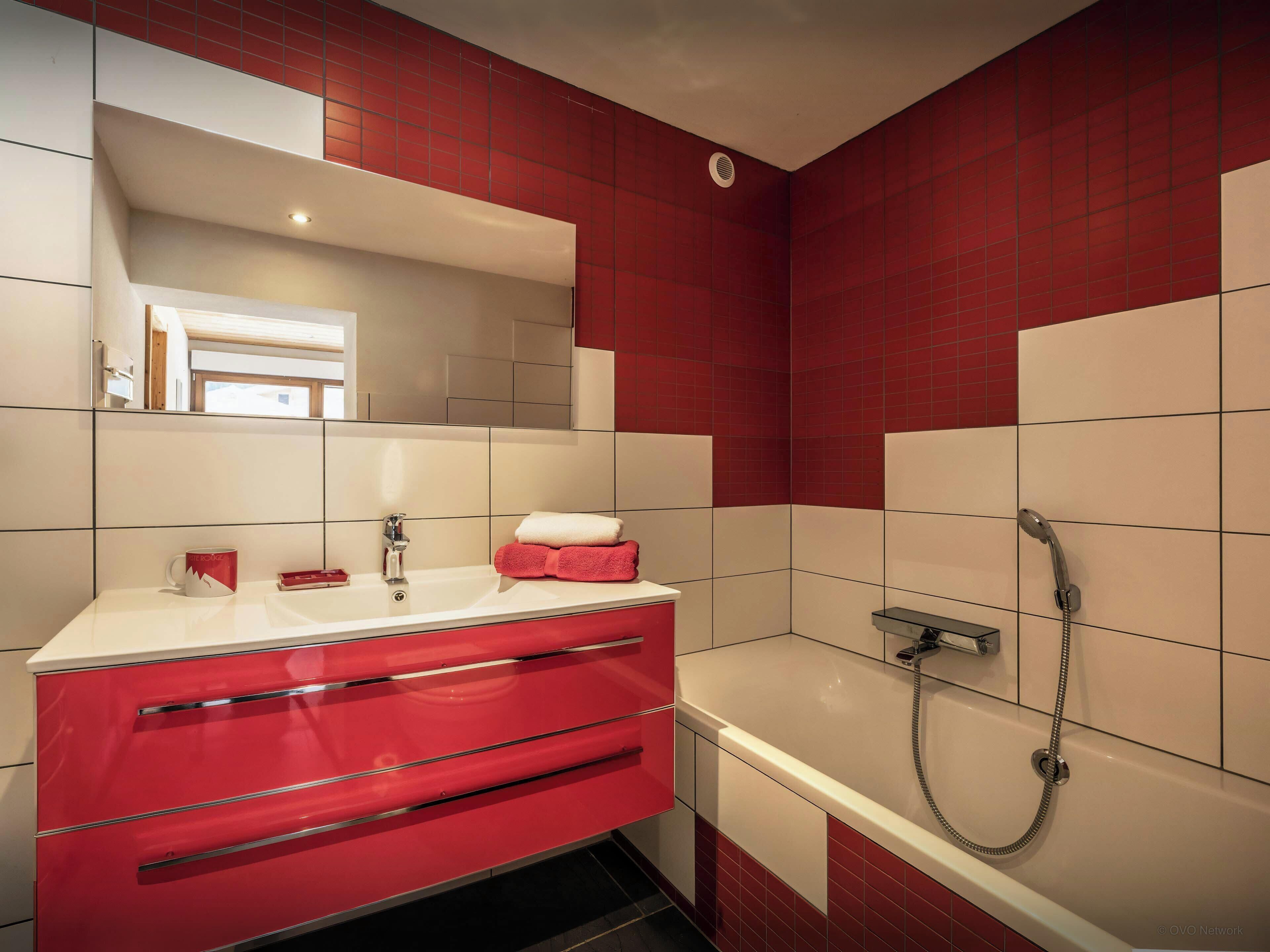Un baño con tocador rojo, un espejo, una bañera y una ducha.