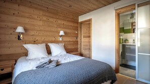 A wooden-paneled bedroom with a bed, two bedside lamps, a nightstand, and a sliding door leading to a bathroom.