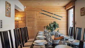 A wooden-paneled dining room with a long table set for a meal, ski poles on the wall, and a window with a view.
