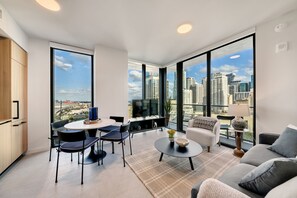 Ein modernes Wohnzimmer mit Blick auf die Stadt, eine Essecke mit Stühlen und Tisch, und ein Sofa.