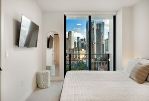 Ein Schlafzimmer mit Bett, Fernseher, Blick auf die Stadt und einem Balkon.