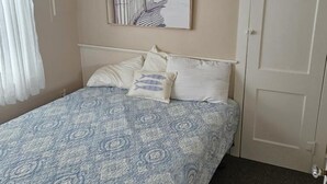 A bedroom with a bed, a painting, a door, and a window with curtains. - Bright & Welcoming 2BR Near Beach, Boardwalk & Local Attractions (Ocean City)