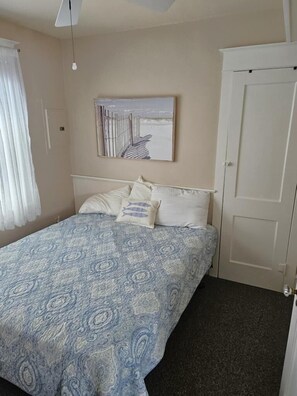Ein Schlafzimmer mit einem Bett, einem Gemälde, einer Tür und einem Fenster mit Vorhängen.
