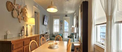 Un comedor con mesa y sillas de madera, un televisor montado en la pared y una ventana con cortinas.