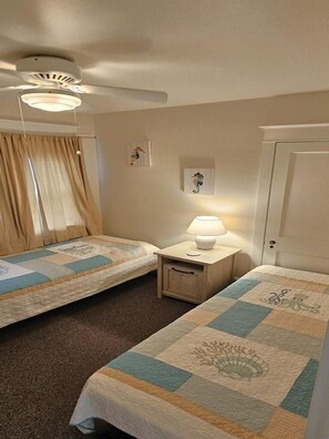 Ein Hotelzimmer mit zwei Betten, einem Deckenventilator, einem Nachttisch mit Lampe und einer Tür.