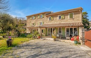 Une maison en pierre avec une allée en gravier, un espace extérieur aménagé pour s’asseoir et des plantes en pot.