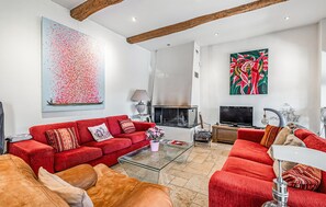 Un salon moderne avec un ensemble de canapés rouges, une cheminée et deux grandes peintures abstraites.