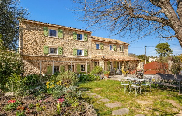 Un bâtiment en pierre doté de nombreuses fenêtres et d’un patio aménagé avec du mobilier d’extérieur.