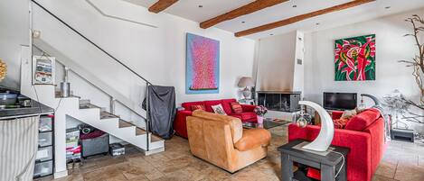 A spacious living area with a staircase, red sofas, a leather armchair, and a fireplace.