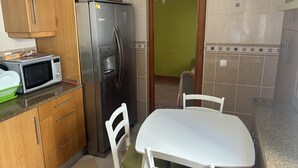 A kitchen with wooden cabinets, a stainless steel refrigerator, a microwave, and a white table with chairs. - Altura verde apartment (Altura)