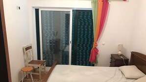 A bedroom with a bed, a chair, a nightstand, a lamp, and a sliding glass door with curtains. - Altura verde apartment (Altura)