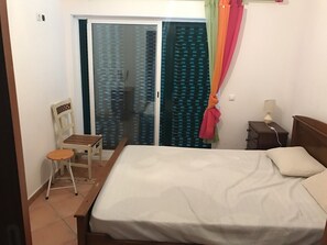 Ein Schlafzimmer mit einem Bett, einem Sessel, einem Nachttisch, einer Lampe und einer Glastür mit Vorhängen.