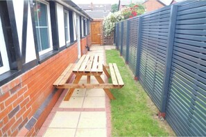 A narrow outdoor patio with a wooden table and benches, surrounded by a brick wall and a metal fence. - The Pavilion (Lytham Saint Annes)