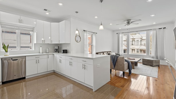 A modern kitchen with white cabinets, a dishwasher, and a dining area with a sofa and table. - Massive 4-bedroom, 3-bathroom duplex apt with garage parking in Jersey City (Jersey City)