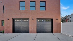 A red brick building with two garage doors and a white fence. - Massive 4-bedroom, 3-bathroom duplex apt with garage parking in Jersey City (Jersey City)