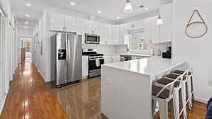 A modern kitchen with stainless steel appliances, white cabinetry, and a central island with bar stools. - Massive 4-bedroom, 3-bathroom duplex apt with garage parking in Jersey City (Jersey City)