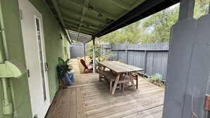 A covered patio with a wooden table and chairs, a door with a window, and a wooden fence in the background. - Hot Tub. A/C. Laundry. 2 Parking Spots. Orchard. (San Diego)