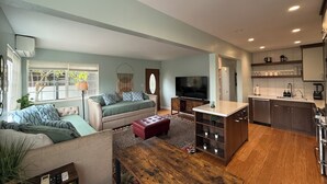 A modern living room with a sofa, a TV, a wooden coffee table, and a kitchen area with cabinets and a sink. - Hot Tub. A/C. Laundry. 2 Parking Spots. Orchard. (San Diego)
