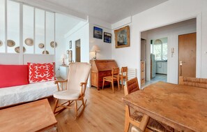 A cozy living room with a wooden dining table, a sofa with a red pillow, and a chair with a white cushion.