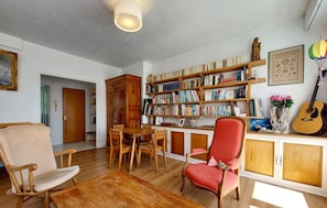 A cozy living room with a wooden bookshelf, a dining area, and a red chair.