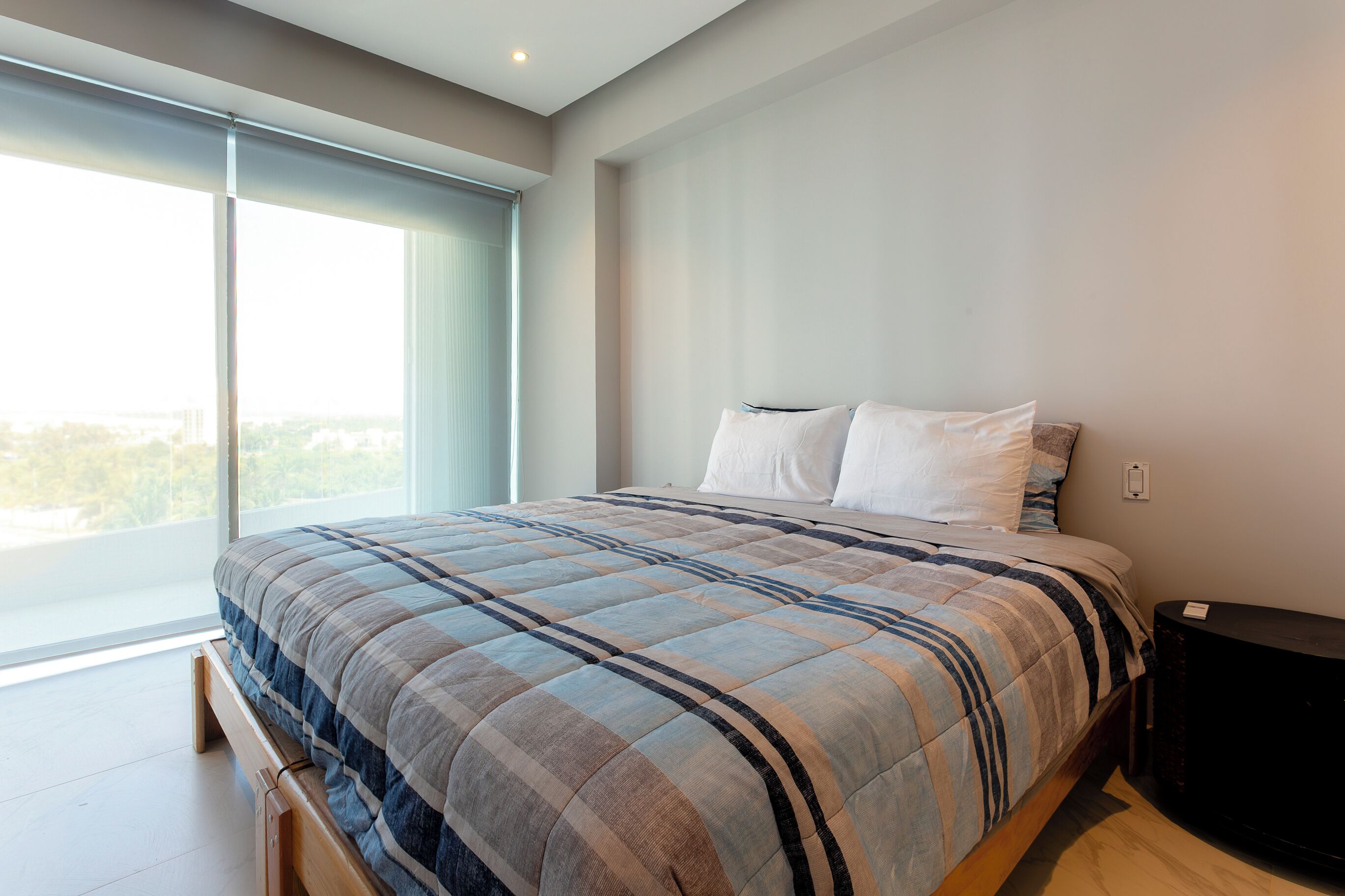 A modern bedroom with a large bed, a window, and a nightstand.