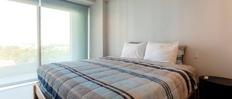 A modern bedroom with a large bed, a window, and a nightstand.
