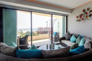 A modern living room with a large glass door leading to a balcony, wicker furniture, and a decorative leaf wall art piece. - Luxury condo in Acapulco Diamante (Acapulco de Juárez)