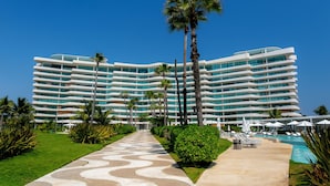Et moderne hotel med pool, palmer og en klar blå himmel.