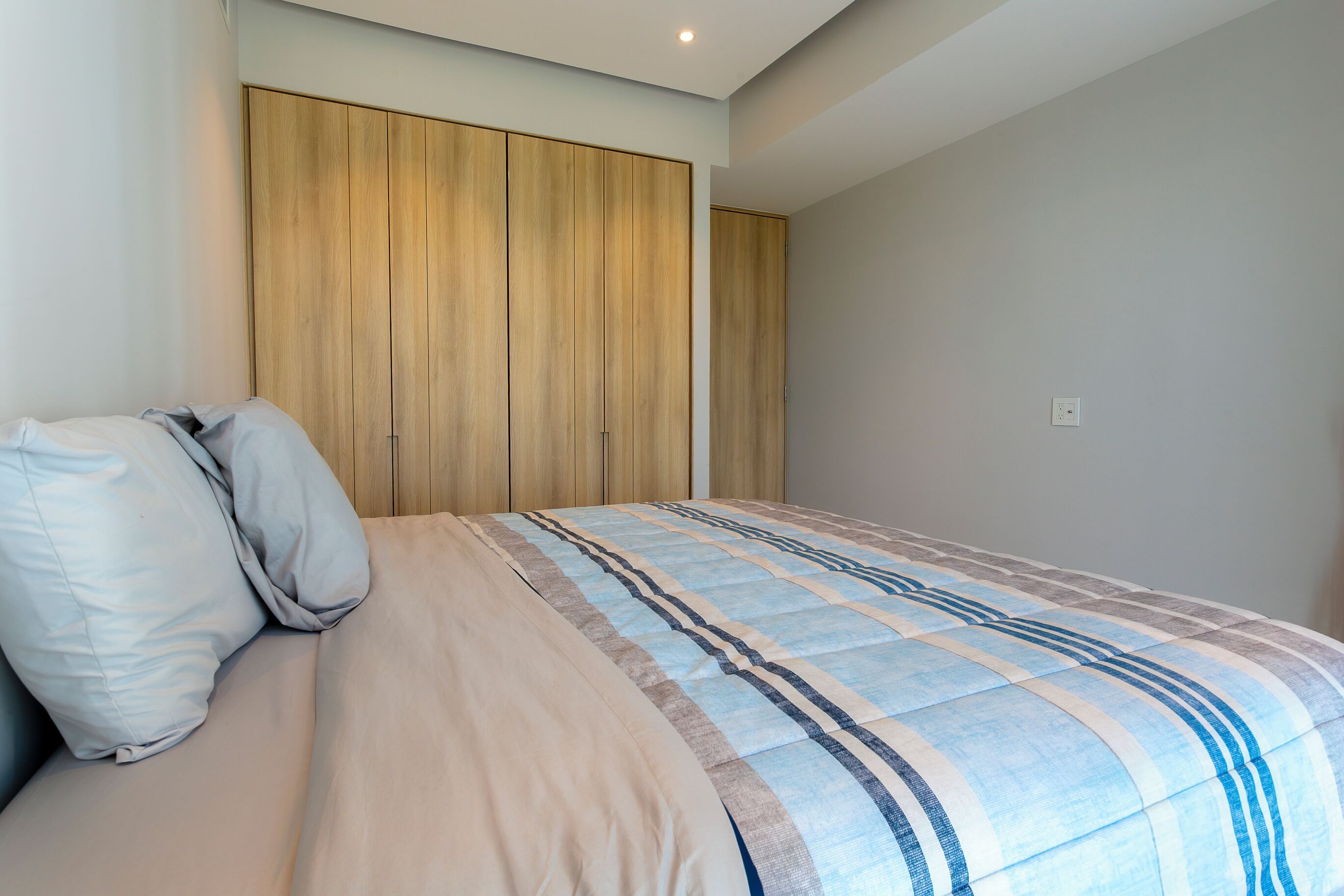 Una camera da letto con un letto, cuscini, un'armadio in legno e una parete di colore chiaro.